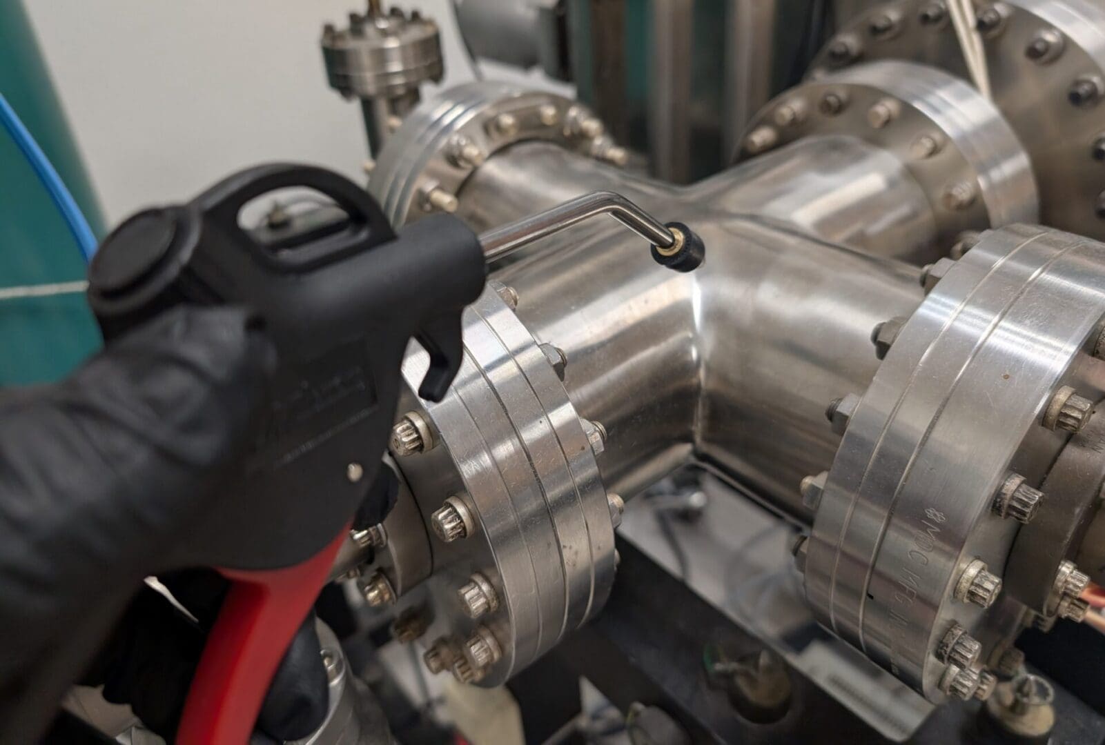 Gloved hand holding air gun near pipe flange